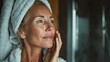 © Johannes - headshot of gorgeous mid age adult 50 years old blonde woman standing in bathroom after shower touching face looking at reflection in mirror doing morning beauty routine older skin care concept no lo