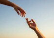 © senyumanmu - Two hands reaching out to each other against a clear blue sky