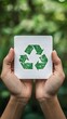 © PinkBirdDesign - Hands Holding White Card with Green Recycling Symbol over Natural Forest Background perfect for environmental awareness campaigns, eco-friendly product branding, sustainability reports
