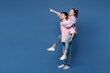 © ViDi Studio - Full body young couple two friends family man woman wearing pink casual clothes together giving piggyback ride to joyful, sit on back point aside isolated on plain blue background. Lifestyle concept.
