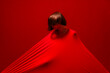 © Studio Marmellata - A woman with short hair is covered by a taut red fabric, creating strong lines and shadows. Her head is tilted down against the vibrant red background. This abstract composition highlights form.