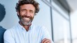 © liliyabatyrova - A man with curly hair and a beard stands confidently with crossed arms outside a modern building. He wears a light shirt and appears to be enjoying his day, showcasing a friendly demeanor.
