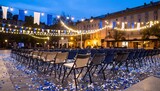 Outdoor event space at dusk with rows of chairs, string lights, and blue and white decorations, ready for a gathering.