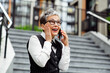 © deagreez - Mature businesswoman conversing on a smartphone outdoors with a joyful expression in an urban setting during spring