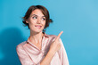 © deagreez - Confident young woman in satin pink blouse smiling and pointing with finger against bright blue background