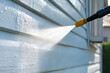 © sornram - A close-up of a pressure washer cleaning a white wooden exterior, showcasing effective dirt removal and the importance of regular maintenance for homes.