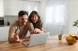 © Goran - Happy couple using credit card for online shopping over laptop at home.