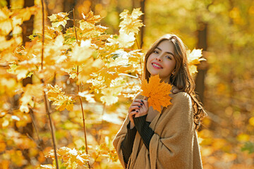 Wall Mural - Autumn woman in golden sunlight. Romantic portrait of stylish girl with leaves. Beautiful woman face in autumn park. Autumn model by falling foliage. Young woman walking through yellow leaves.
