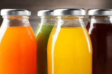 Wall Mural - Tasty juices in glass bottles against blurred brown background, closeup