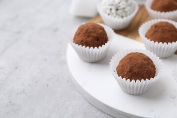 Wall Mural - Delicious homemade candies with cocoa powder and coconut flakes on light grey table, closeup. Space for text
