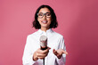 © deagreez - Confident young woman holding a microphone against a pink background, showcasing a stylish and professional demeanor in formal attire