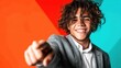 © Freshpixel - A charming young man with curly hair smiles and points directly at the camera, radiating positivity and energy against a brightly colored backdrop, inviting connection with viewers.