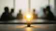 © buraratn - Glowing light bulb symbolizes innovation and creativity, set against blurred background of business meeting. warm light contrasts with cool tones of environment, evoking inspiration
