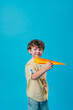 © lithiumphoto - Little boy holding paper plane standing over blue background