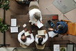 © pressmaster - Group of middle aged and senior multiethnic doctors and one middle aged Caucasian man sitting around table discussing medical documents and using laptop during meeting, top view
