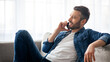 © Prostock-studio - Communication concept. Relaxed middle-aged man sitting on sofa in living room, having conversation on mobile phone with friend or lover and looking at copy space, home interior
