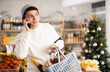 © JackF - Man in sweater making mobile phone call near food shelves in Christmas supermarket. Guy chooses food and answers the phone.
