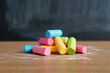 © ADPShapla - Pile of colorful chalk sticks on a wooden surface against a blackboard