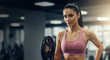 © Vasiliy - Woman in pink sports bra holding weight plate with confident hand-on-hip pose in gym. Athletic confidence content for fitness center promotional banners