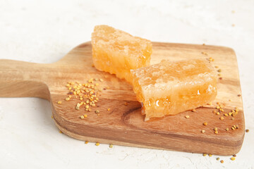 Wall Mural - Wooden board with fresh honeycombs and bee pollen on light background, closeup