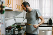 © TrueShot | Westend61 - Mid adult man cooking while video conferencing on laptop at home
