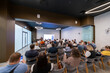 © Anton Gvozdikov - People attending a professional presentation in a modern conference room with a speaker presenting on a screen.