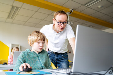 Professor assisting boy with coding in laptop at desk