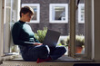 © TrueShot | Westend61 - Woman sitting at the window at home using laptop