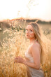 © Mariia Andreeva - Slavic woman with long white hair standing in golden grass field, natural beauty and ethnic portrait in summer countryside landscape at sunset.