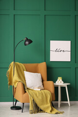 Poster - coffee table with lamp and blanket on armchair near green wall