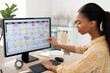 © AI_images_for_people - Young adult African-American woman setting up a content calendar for digital campaigns, organizing ideas by month