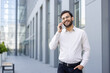 © Liubomir - Smiling professional talking on the phone outdoors near modern office building