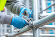 © venusvi - A construction worker wearing gloves assembles scaffolding using a wrench, highlighting safety and industry tools.
