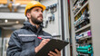 © venusvi - A technician examines electrical control panels with a clipboard while wearing safety gear in an industrial setting.