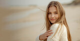 Magnificent young girl on seashore in cold windy day. beautiful young woman with long, wind-swept blonde hair, looking over her shoulder directly at the camera. She has a subtle. copy space