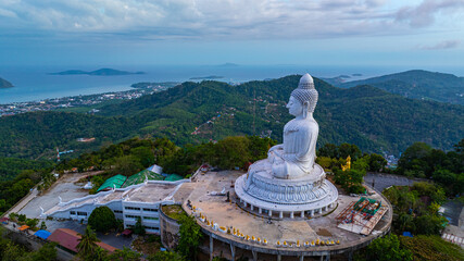 Wall Mural - A breathtaking aerial view of the iconic Big Buddha statue overlooking the Andaman Sea in Phuket, Thailand, captured during a vibrant sunset. The golden sky reflects on the water, majestic hilltop