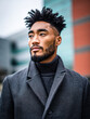 © Kowit - A stylish man in a textured coat stands outdoors, showcasing a modern hairstyle against a blurred urban background.