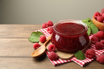 Wall Mural - Tasty jam, fresh ripe raspberries and leaves on wooden table, closeup. Space for text