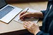 © (JLco) Julia Amaral - Person writing in a notebook with a laptop on a wooden desk