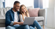 © Prostock-studio - Cheerful Millennial Mixed Couple Spending Time With Laptop At Home, Happy Young Interracial Lovers Sitting On Floor With Computer, Watching Movies Or Shopping Online Together, Free Space