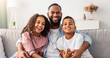 © Prostock-studio - Happy Loving Family. Portrait of cheerful smiling African American dad embracing his little children, sitting on couch, looking at camera. Girl, boy and man hugging, enjoying time together