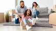 © Prostock-studio - Moving Into New Apartment. Portrait of positive black family of three people having fun together in new flat, unpacking stuff, cheerful father riding his happy little daughter in carton box