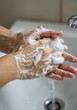 © rudy2101 - Soapy hands under a faucet above a white sink with water running