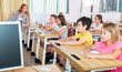 © JackF - Schoolkids sitting at desks in classroom. They're listening to feamle teacher who's explaining them lesson information.