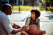 © Davor - Father teaching son how to play basketball on outdoor court at sunset