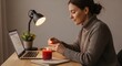 © Elva - Serene woman lighting a candle at her desk creating a cozy atmosphere for focused work or relaxation with a laptop nearby