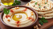 © Bricio - A bowl of hummus with olive oil and paprika served with pita bread and a bulb of garlic in the back