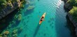 © Vadym - Lone kayaker paddles bright orange kayak through tranquil turquoise lake water. Surrounded by rocky shores with green vegetation. Sunlight reflects on water surface creating ripples. Top-down