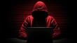 © AndyAziz - Mysterious figure wearing a red hoodie working on a laptop in a dark environment with dramatic lighting
