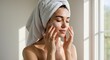 © Mosalah - Woman towelwrapped head applying facial cream with closed eyes near a window